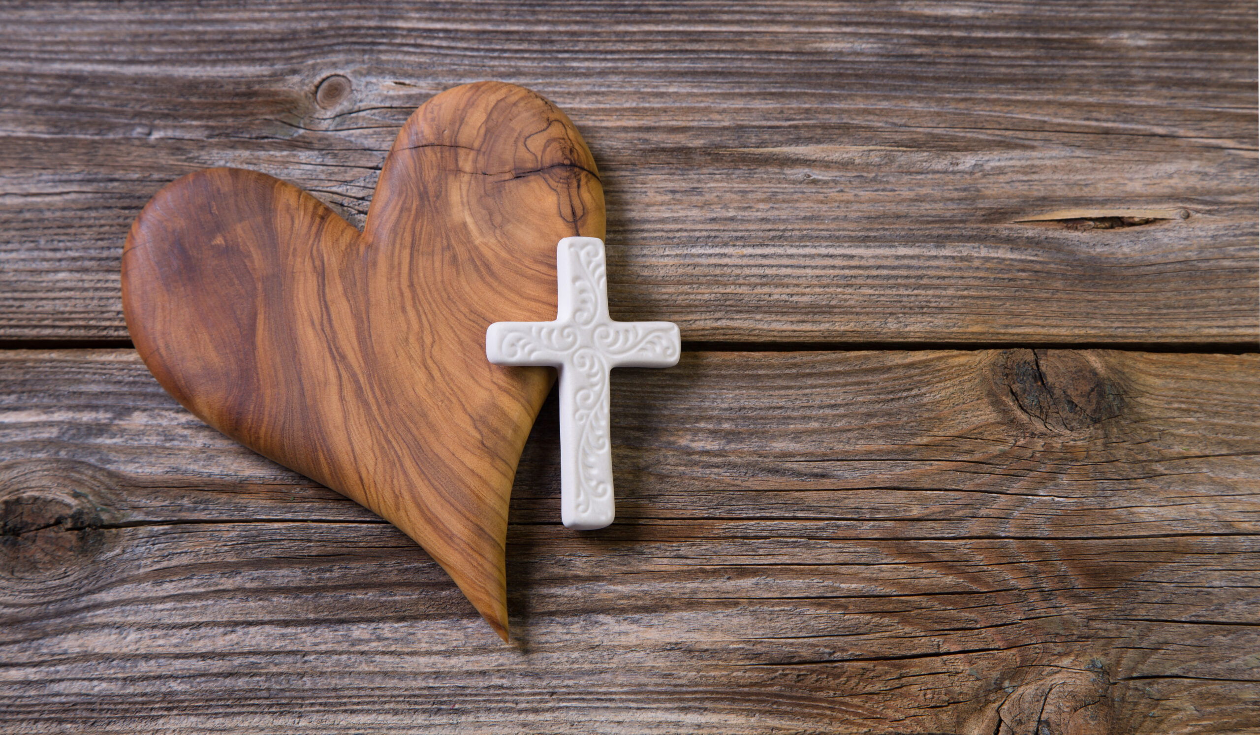 Wooden background with olive heart and white cross for an obitua